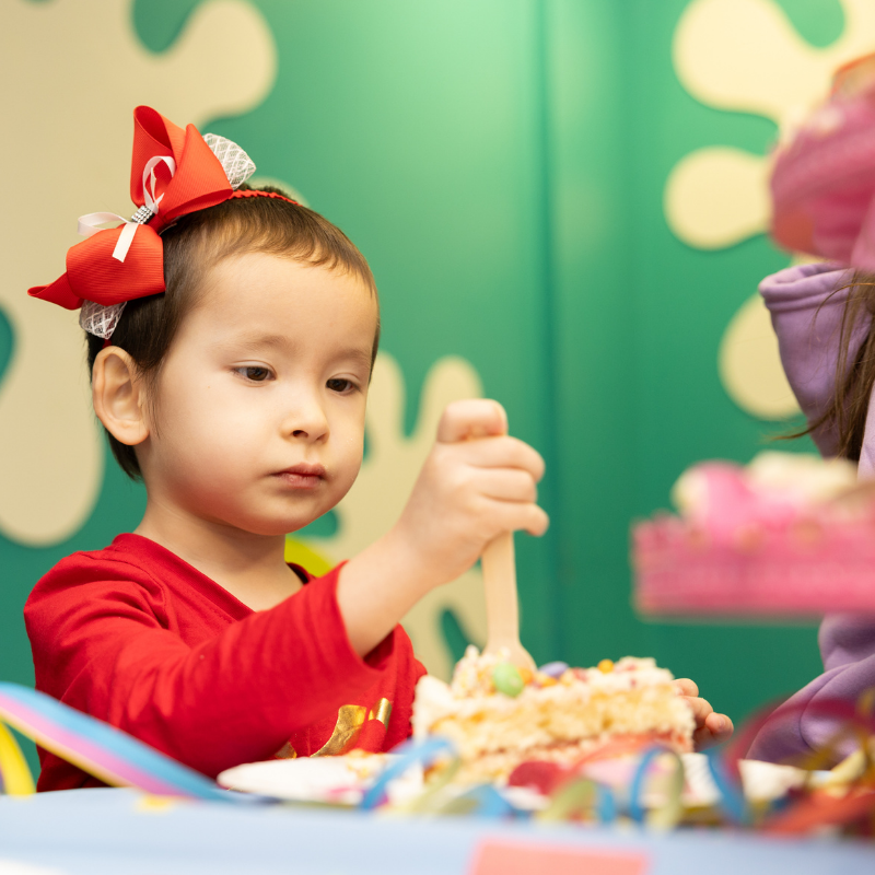 Young child in red with birthday bow enjoying party decorations and cake