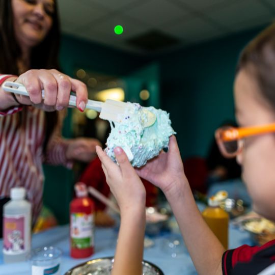 Children decorating a messy blue-green cake with frosting