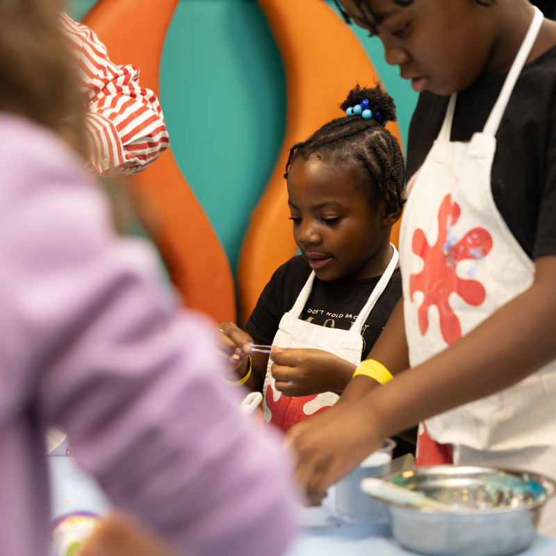 Child in apron concentrating on cooking activity with colorful background