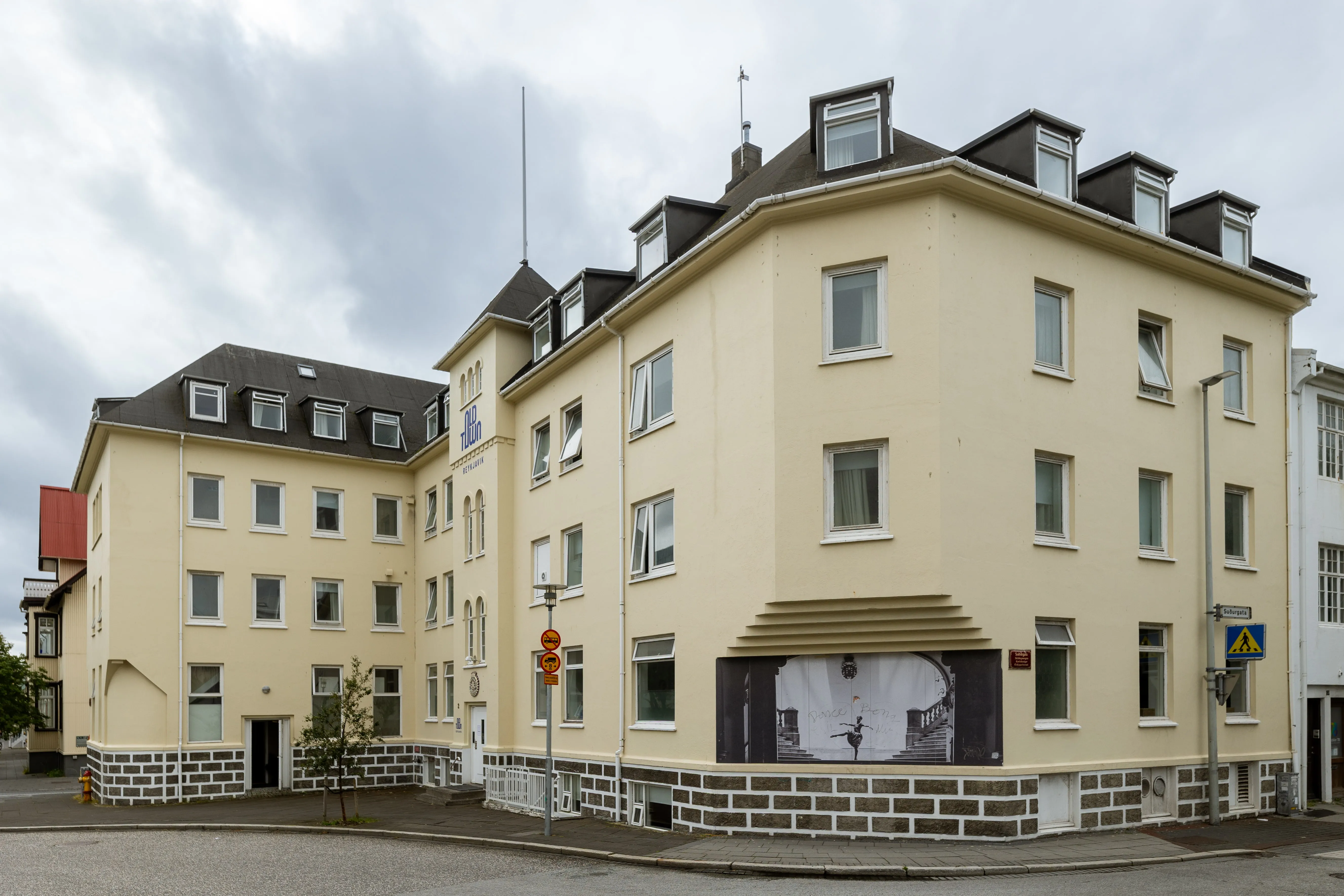 Exterior view of a beige multi-story Old Town Reykjavik building with black roof windows and a mural of a ballerina on the corner wall.