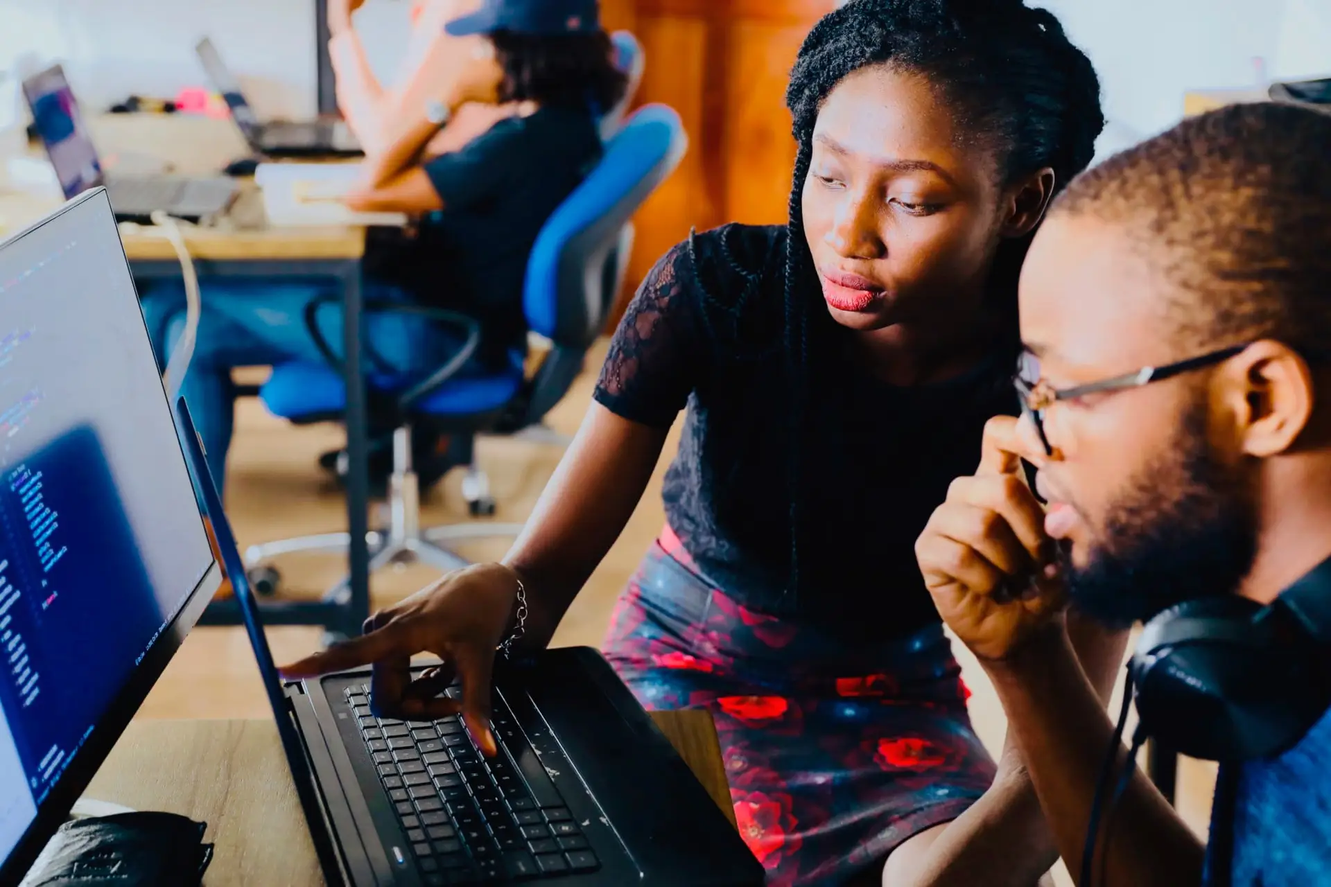 Two people collaborating at a computer, with one person pointing at the laptop screen while the other listens thoughtfully