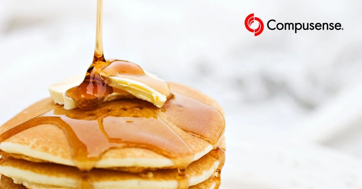 A stack of golden pancakes with maple syrup being drizzled from above, capturing the syrup mid-pour.