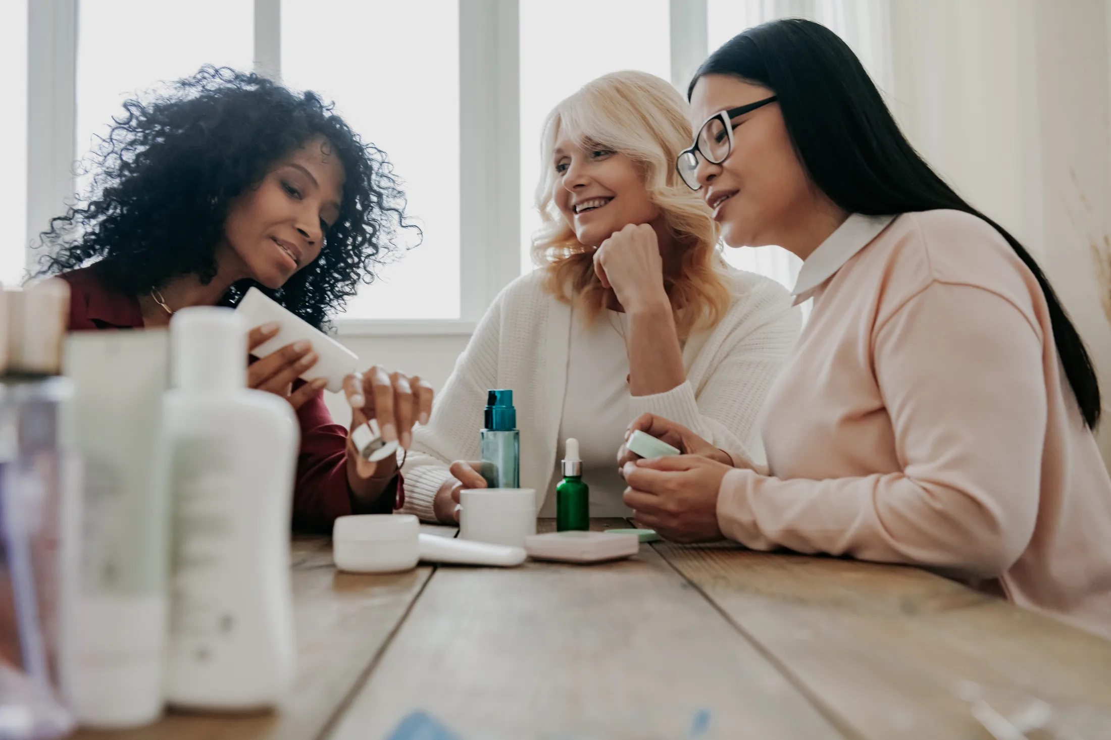 Three happy women testing beauty products at a desk.