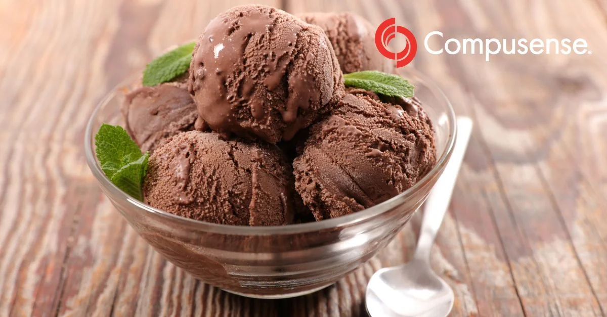 Scoops of chocolate ice cream garnished with fresh mint leaves in a clear glass bowl.