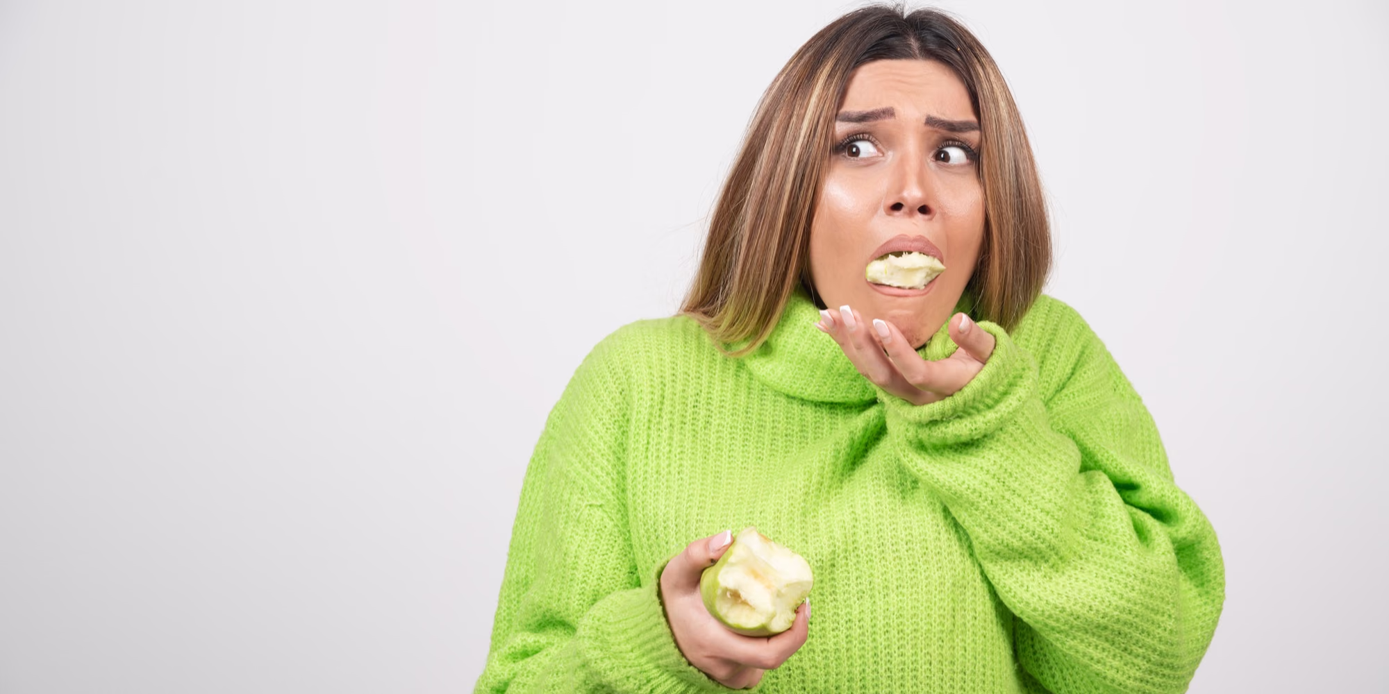 Woman spitting out green apple in green sweater.