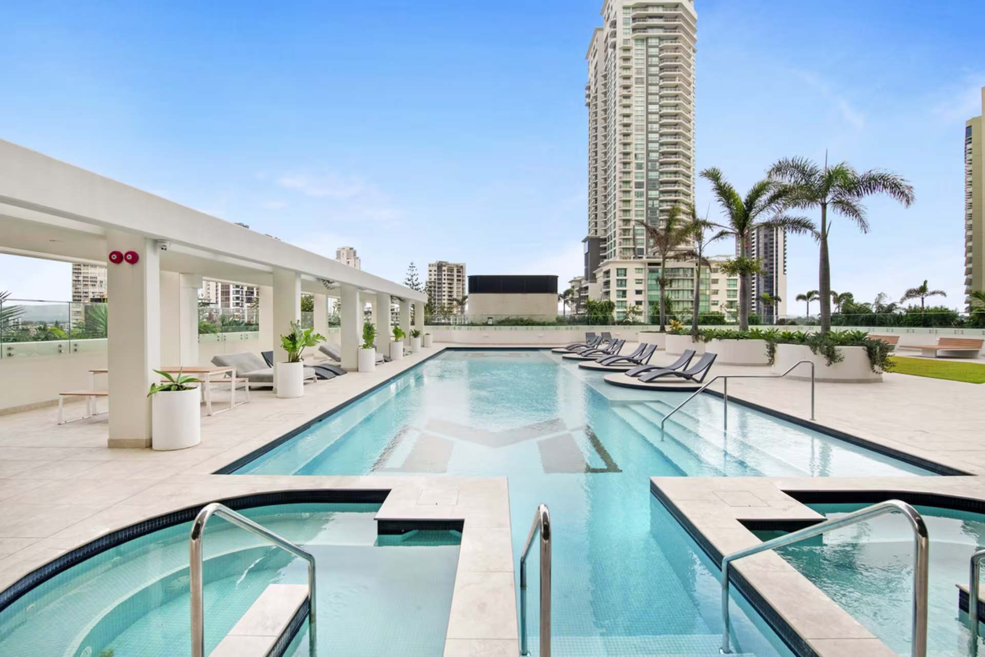 Modern rooftop pool at a Gold Coast Airbnb management apartment, featuring sun loungers, spa access, and city skyline views.