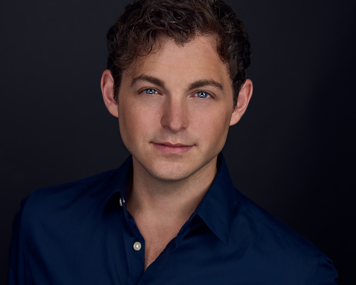Actor headshot of Chris, facing camera with navy shirt on dark background