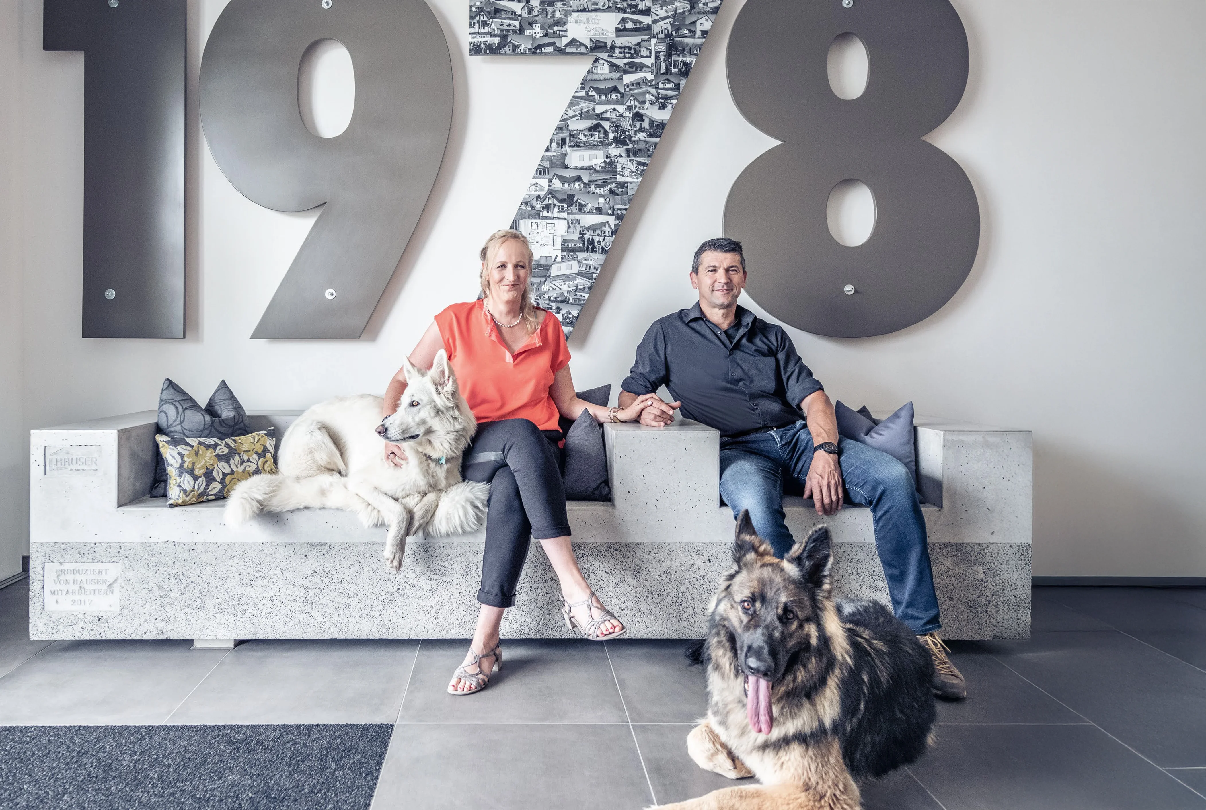 Simone Hauser-Banholzer und Rainer Banholzer sitzend auf Steinsofa mit den Hunden in der Firmenzentrale.