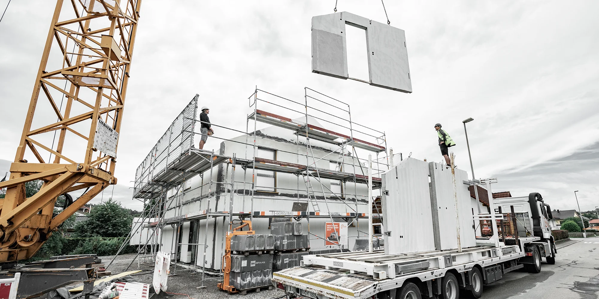 Hauswand wird auf Baustelle von Kran von LKW an seine Position gehoben.