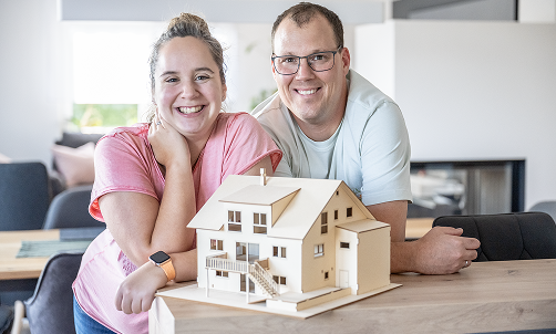 Frau und Mann in ihrer Küche vor einem Modell ihres Hauses.
