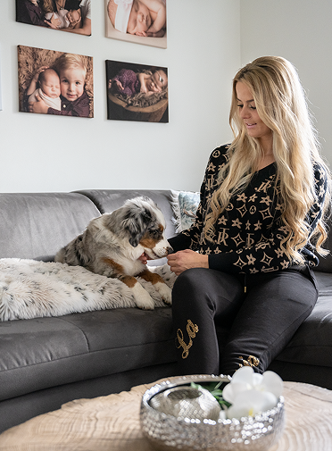 Frau streichelt ihren Hund Zuhause auf dem Sofa.