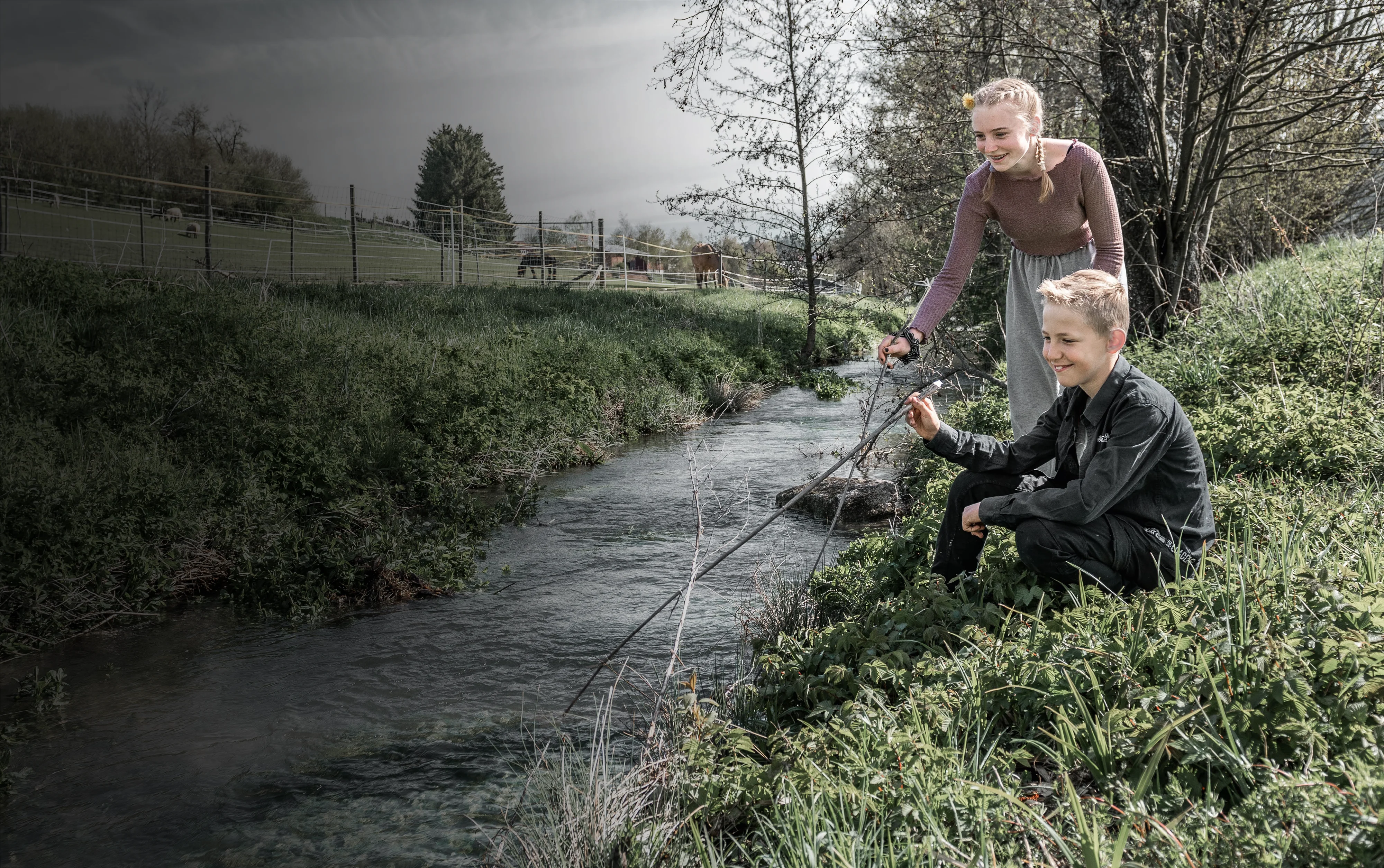 Kinder, die mit Stecken an einem Bach spielen.
