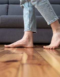 Nahaufnahme Beine inJeans die barfuß auf Holzfußboden im Wohnzimmer laufen.