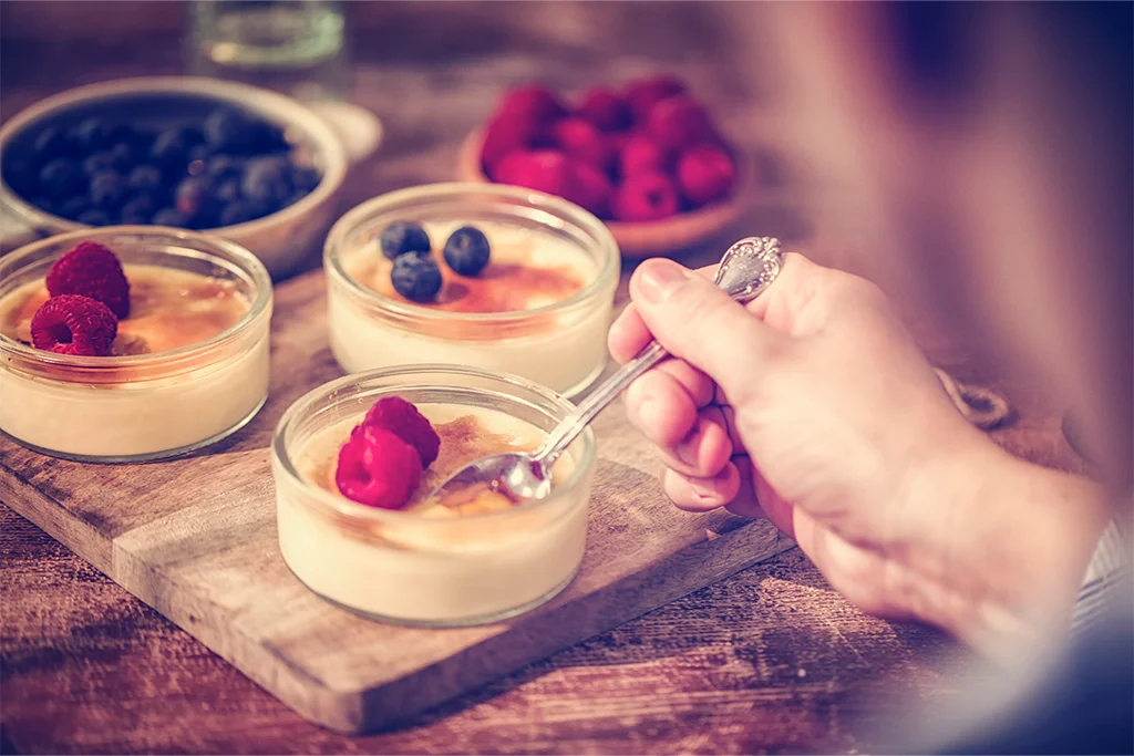 Nahaufnahme Crème brûlée wird gelöffelt mit Himbeeren und Heidelbeeren.