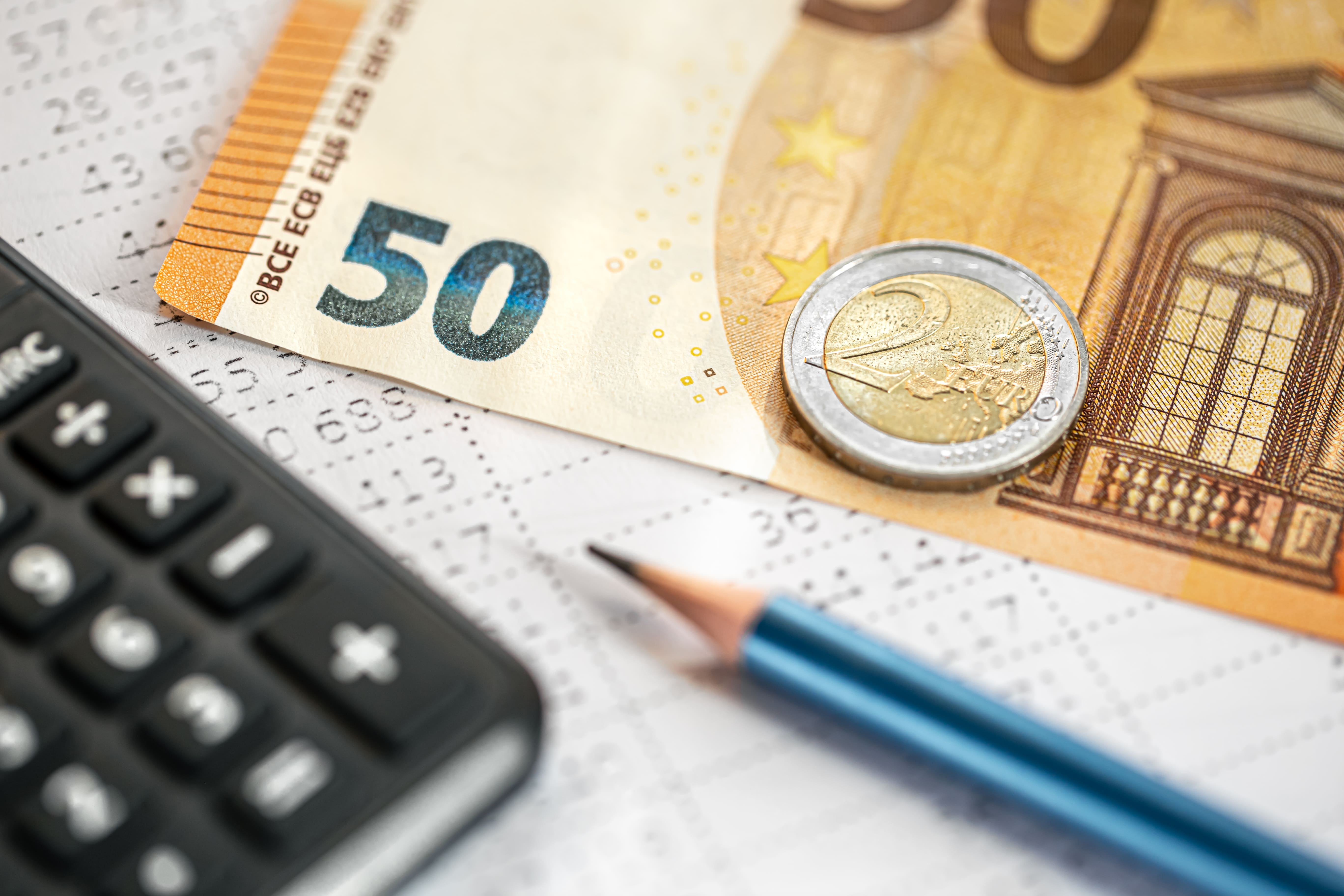 Taschenrechner, Euro-Geldscheine und Münzen auf Finanzunterlagen.