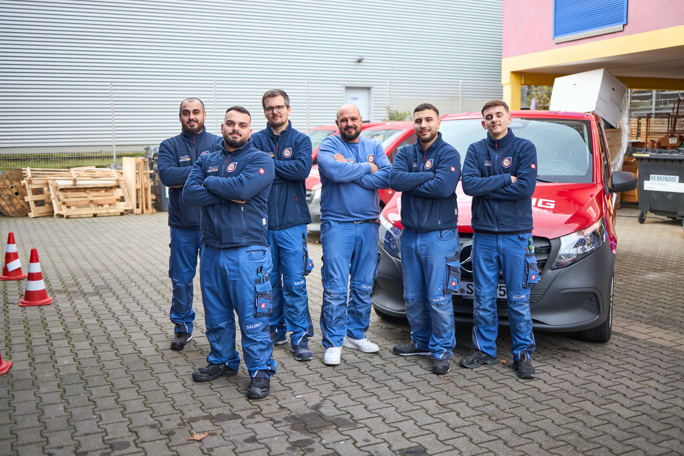 Fünf Handwerkerinnen und Handwerker in Arbeitskleidung gehen gemeinsam mit Werkzeugen aus einer Werkstatt.