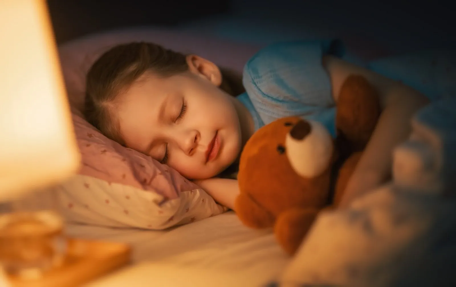 girl sleeping in bed with teddy bear
