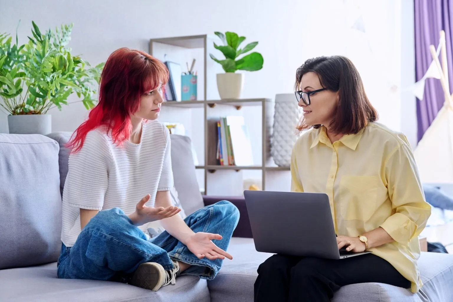 two women sitting on a couch with a laptop