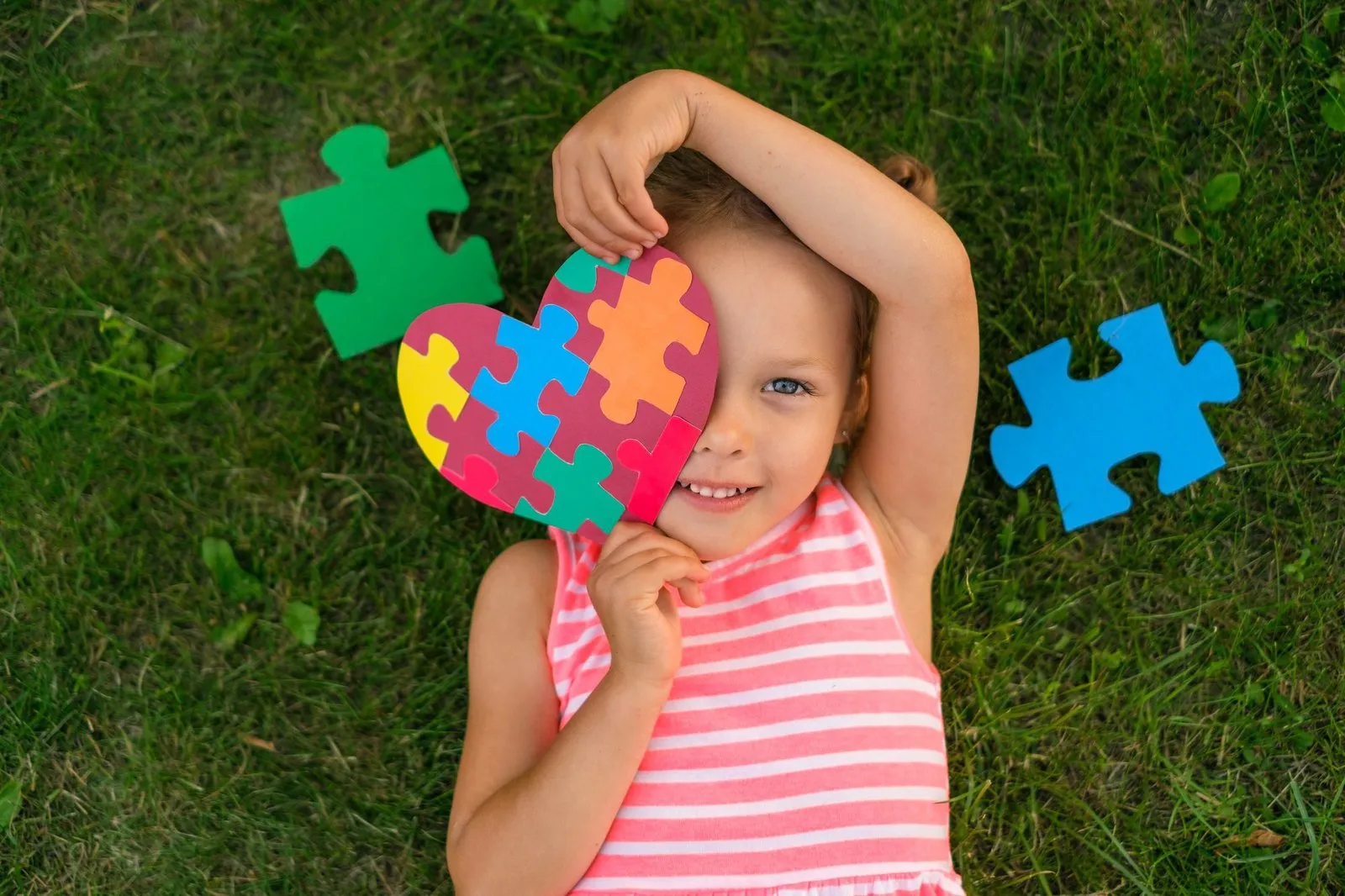 a girl lying on grass holding a heart shaped puzzle piece