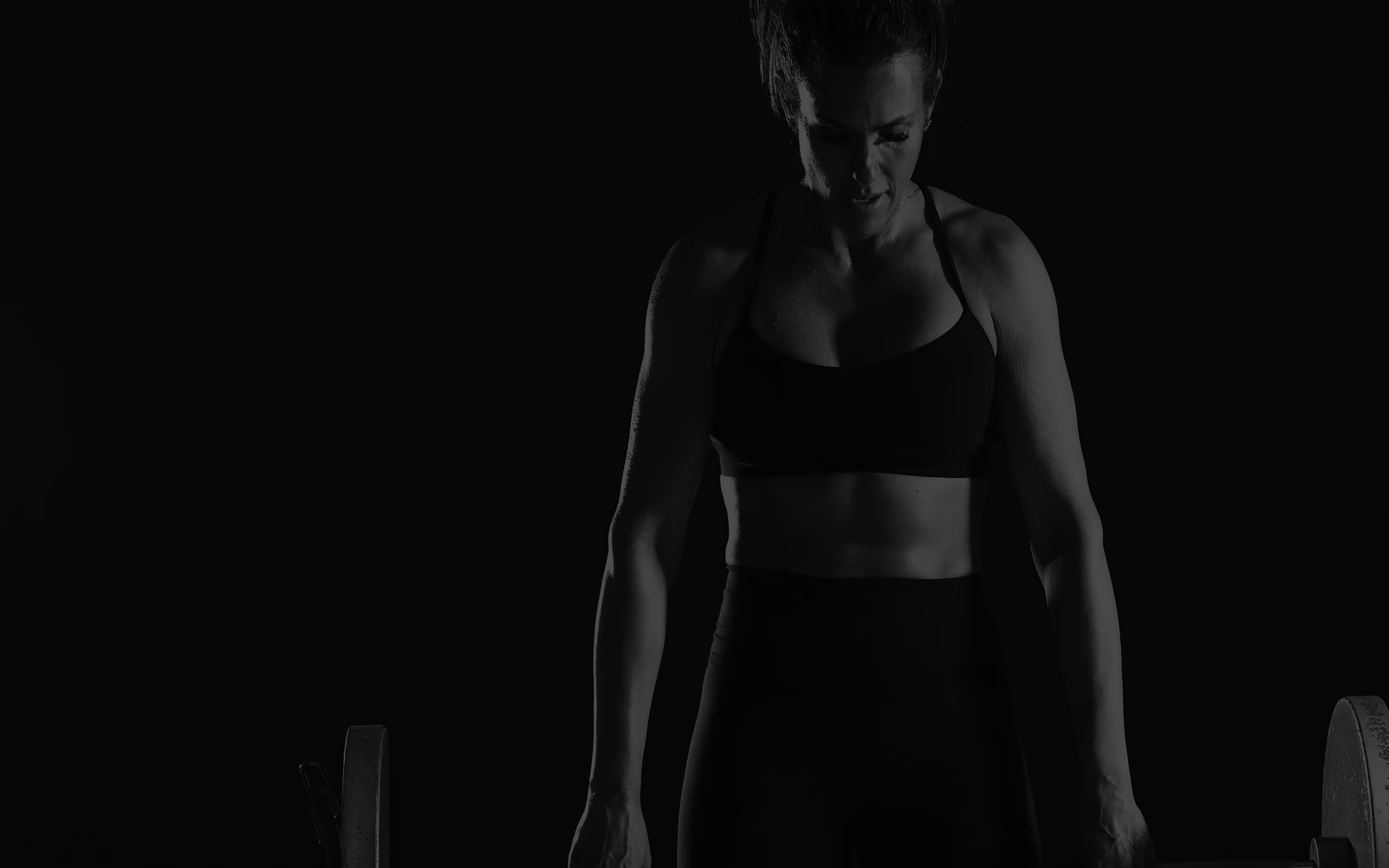 A woman in a sports bra top and shorts holding a barbell.