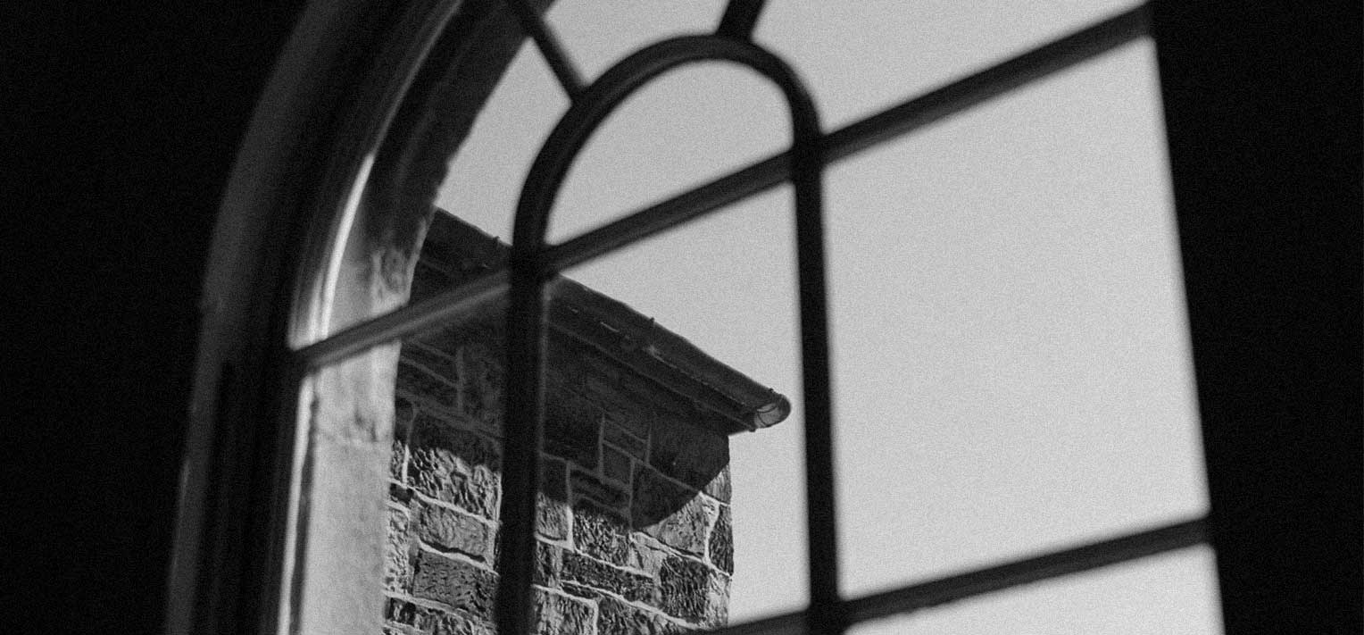 Black and white view through an arched window showcasing a stone building wall and clear sky.