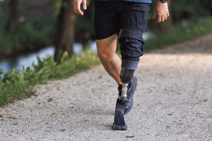 Man walking on a gravel path with a transtibial prosthetic leg and running blade foot.