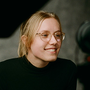 Glimlachende vrouw met bril kijkt richting camera in een studio-opname setting.
