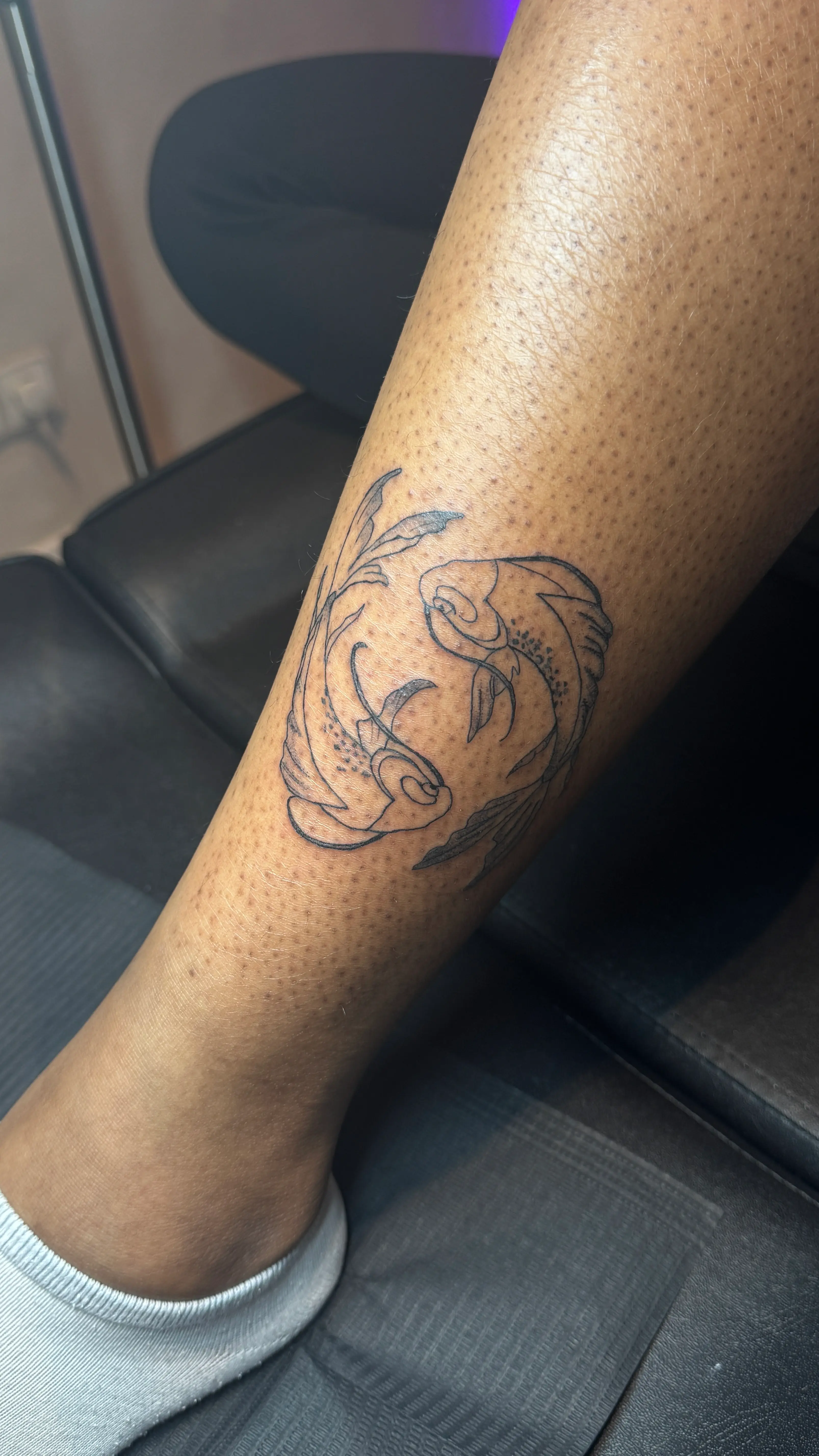 Frisches Finelinetattoo eines Gesichtsprofils auf dem Schienbein einer Person mit dunkler Haut, fotografiert im Tattoo-Studio.