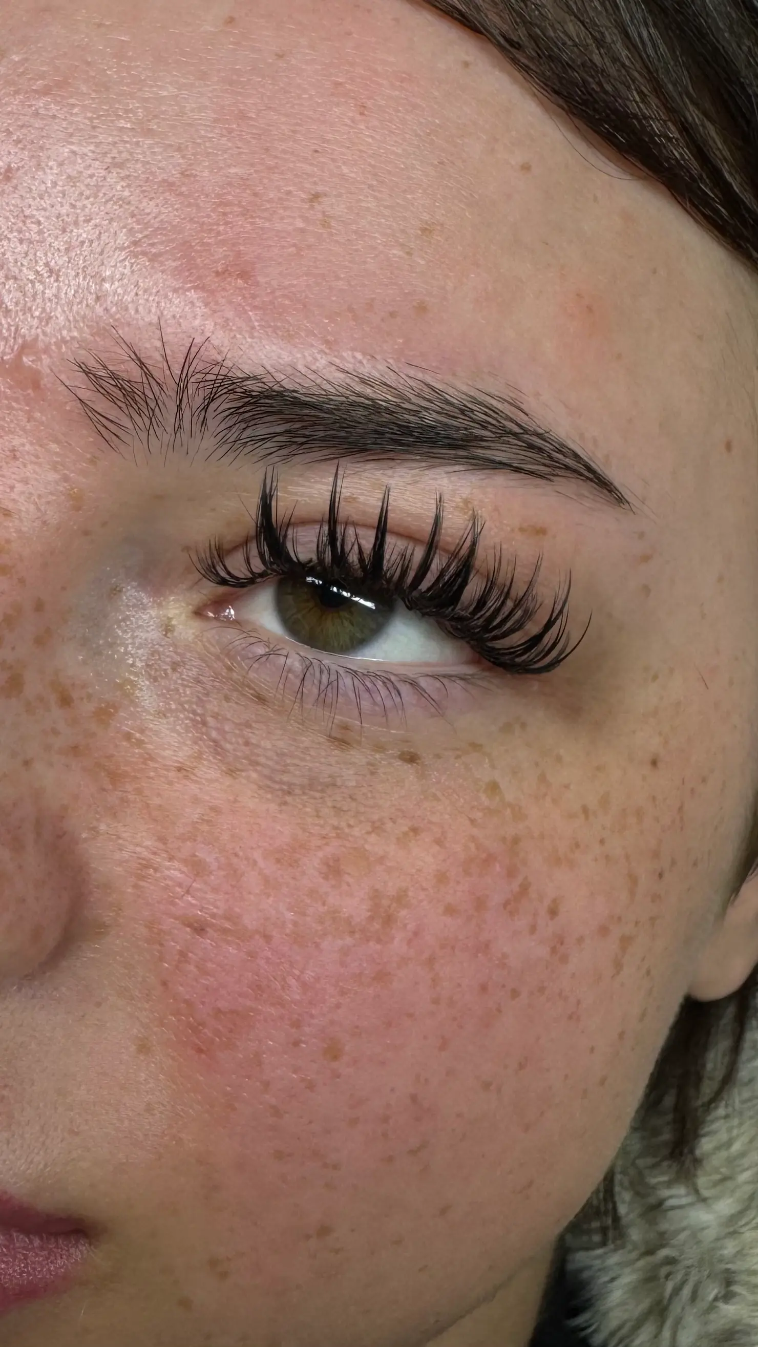 Nahaufnahme eines Auges mit langen, gestylten Wimpern und natürlichen Sommersprossen – Lash Extensions von I AM A PRIORITY