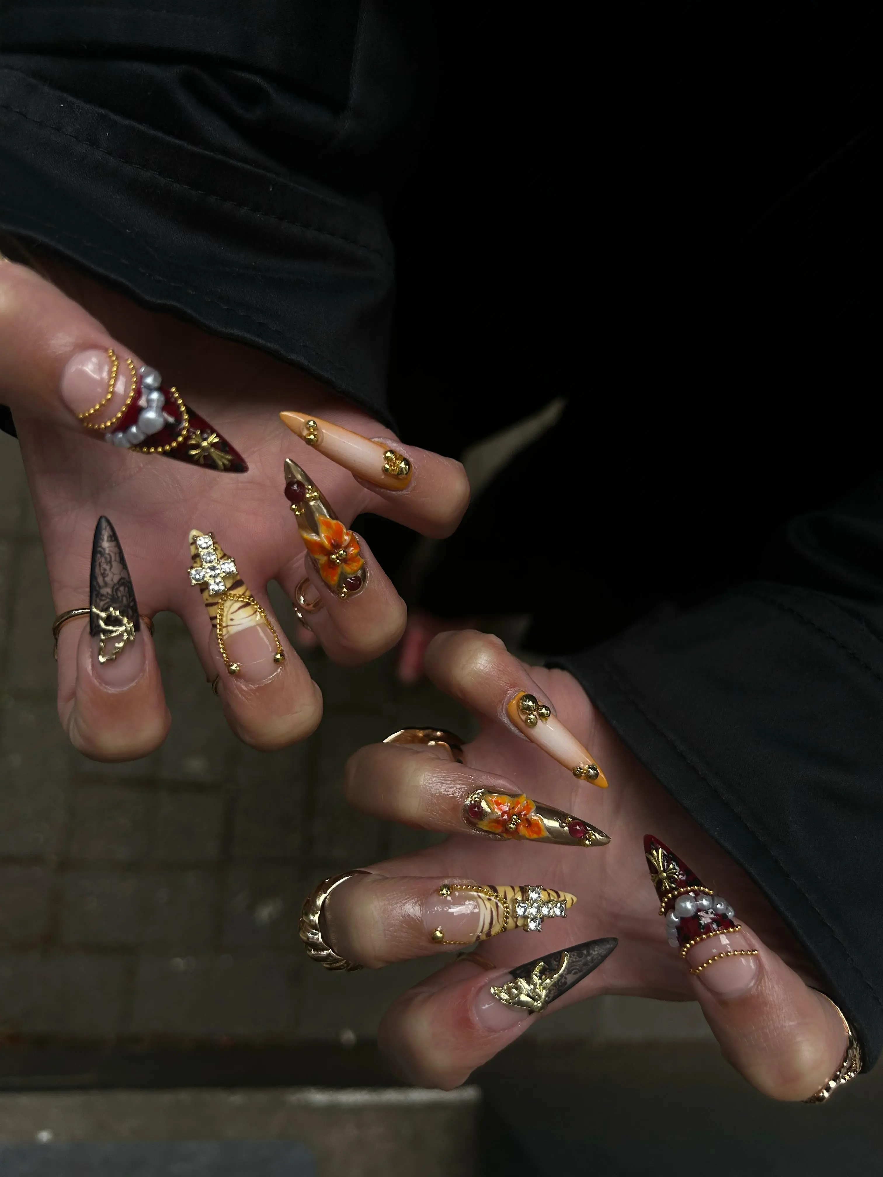 Lange, spitz zulaufende Nägel mit auffälligem herbstlichen Design in Braun- und Goldtönen, verziert mit Glitzer und Blattmotiven.