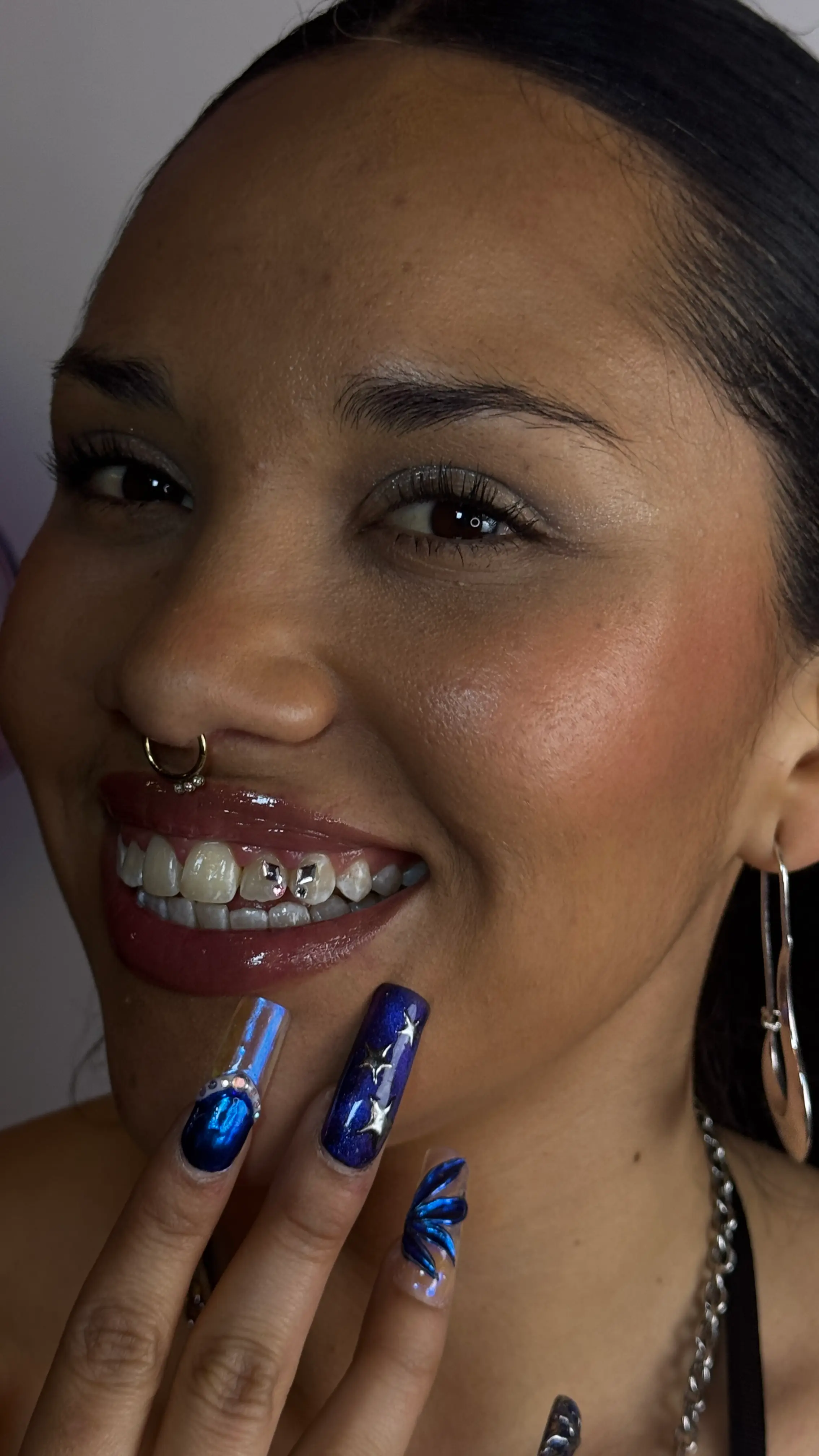 Frau mit Tooth Gems und auffälligem blauen Nageldesign lächelt in die Kamera