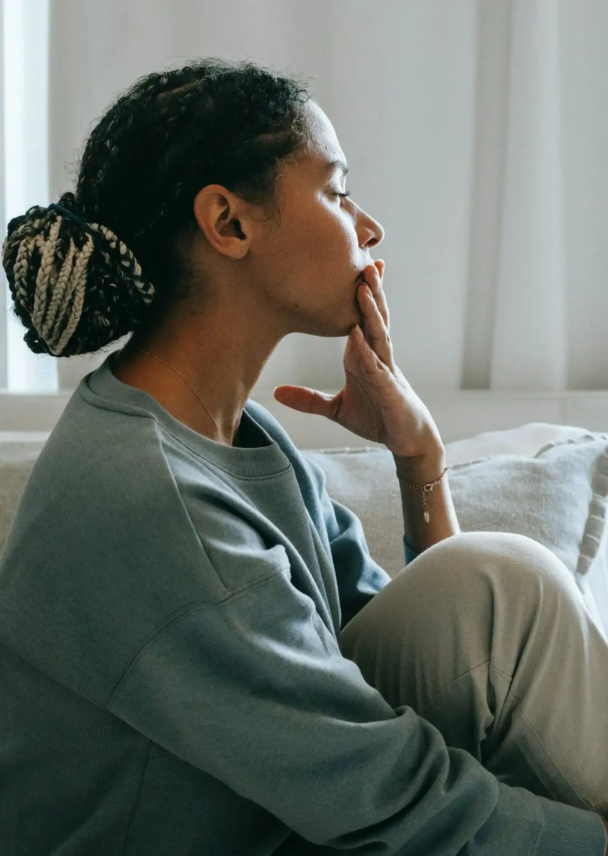 A woman sitting on the sofa, with her hand placed lightly over her chin and mouth