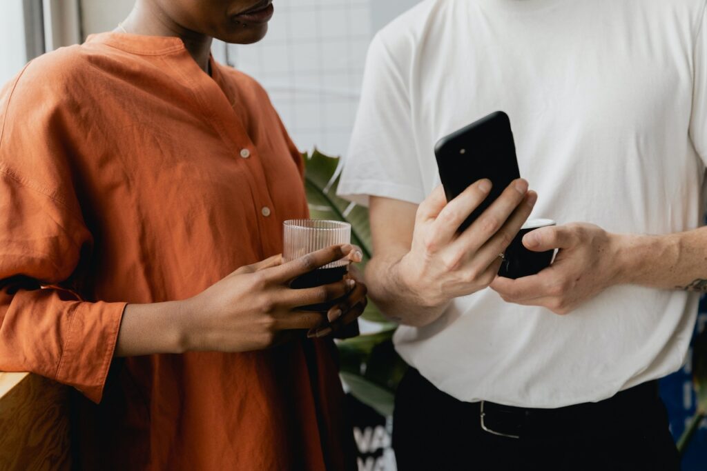 Main in white t-shirt holds phone towards a women in orange blouse holding a glass cup