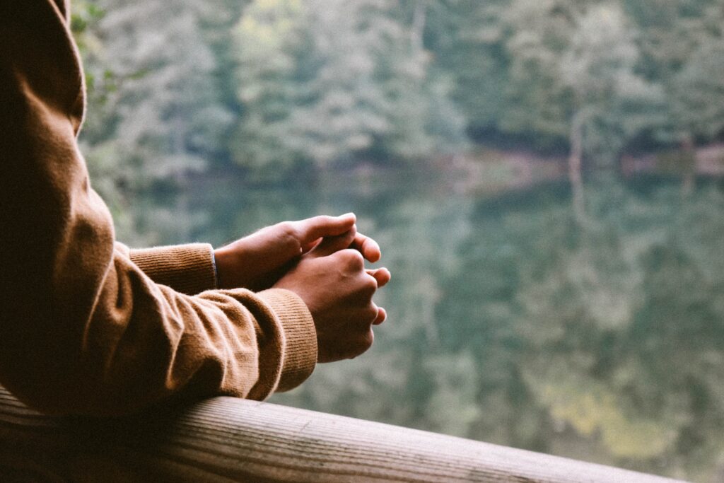 A persons arms resting on a handrail as they look over a lake and forested area