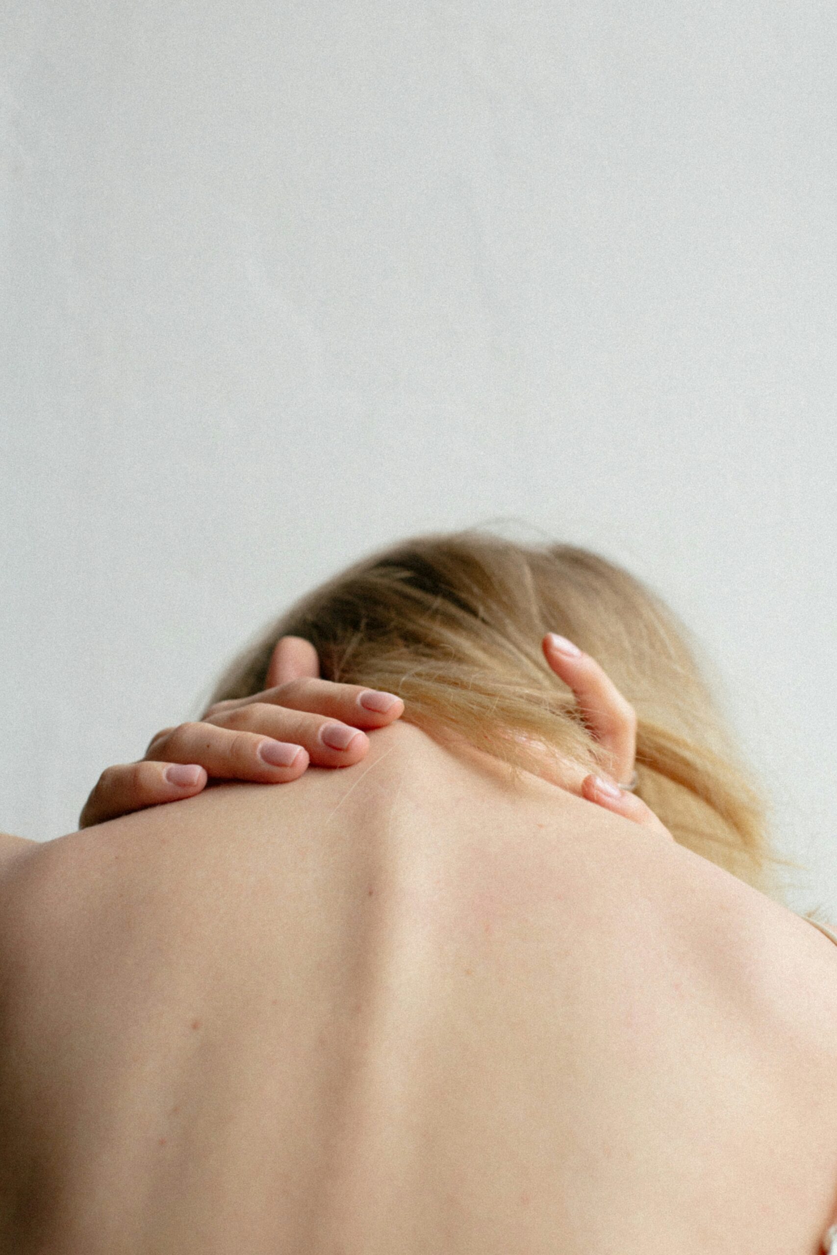 A person leaning forward clutches their neck in pain