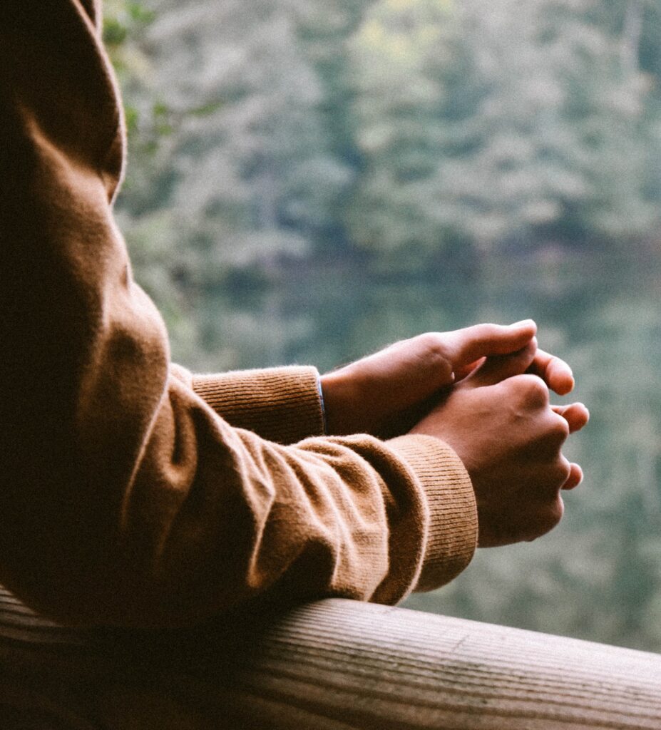 A pair of hands resting on a rail, with the person overlooking a lake