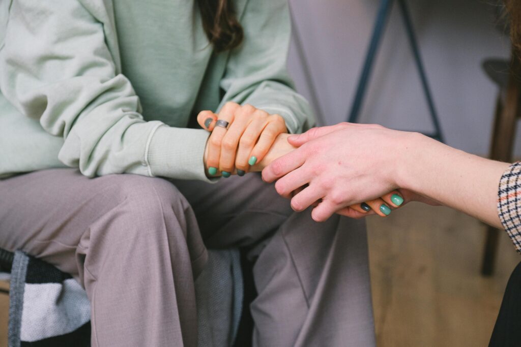 Two people sitting down facing each other, with one holding the hand of the other in support