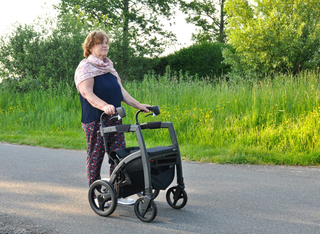 An elderly woman using a wheeled walker to assist movement