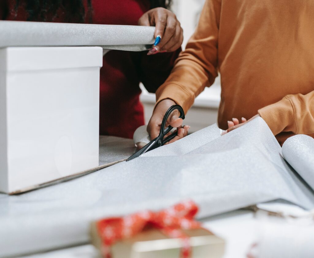 Two people wrapping a large gift with wrapping paper