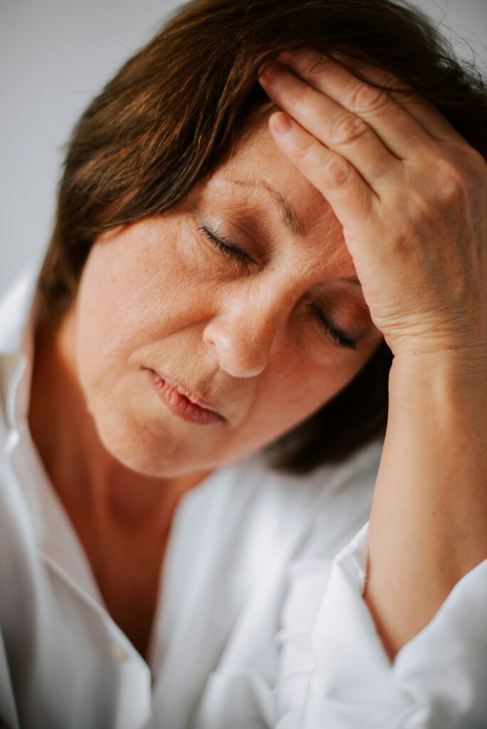 A close-up of a woman with her palm on her forehead in pain