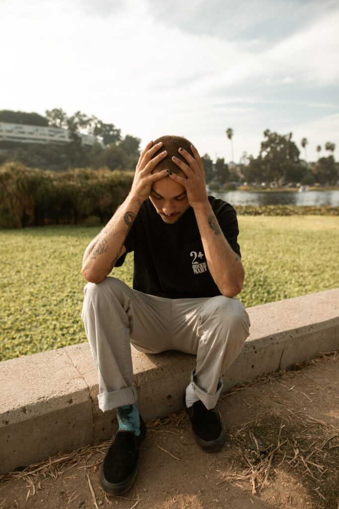 A man sits on wall in the park with his head in his hands