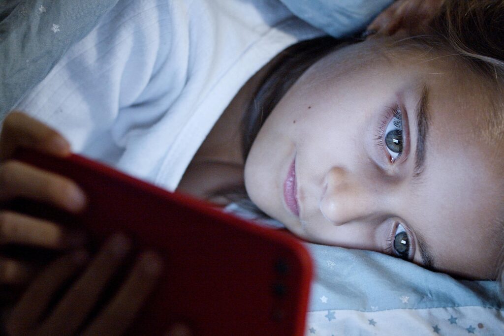 A child in bed watching videos on their phone