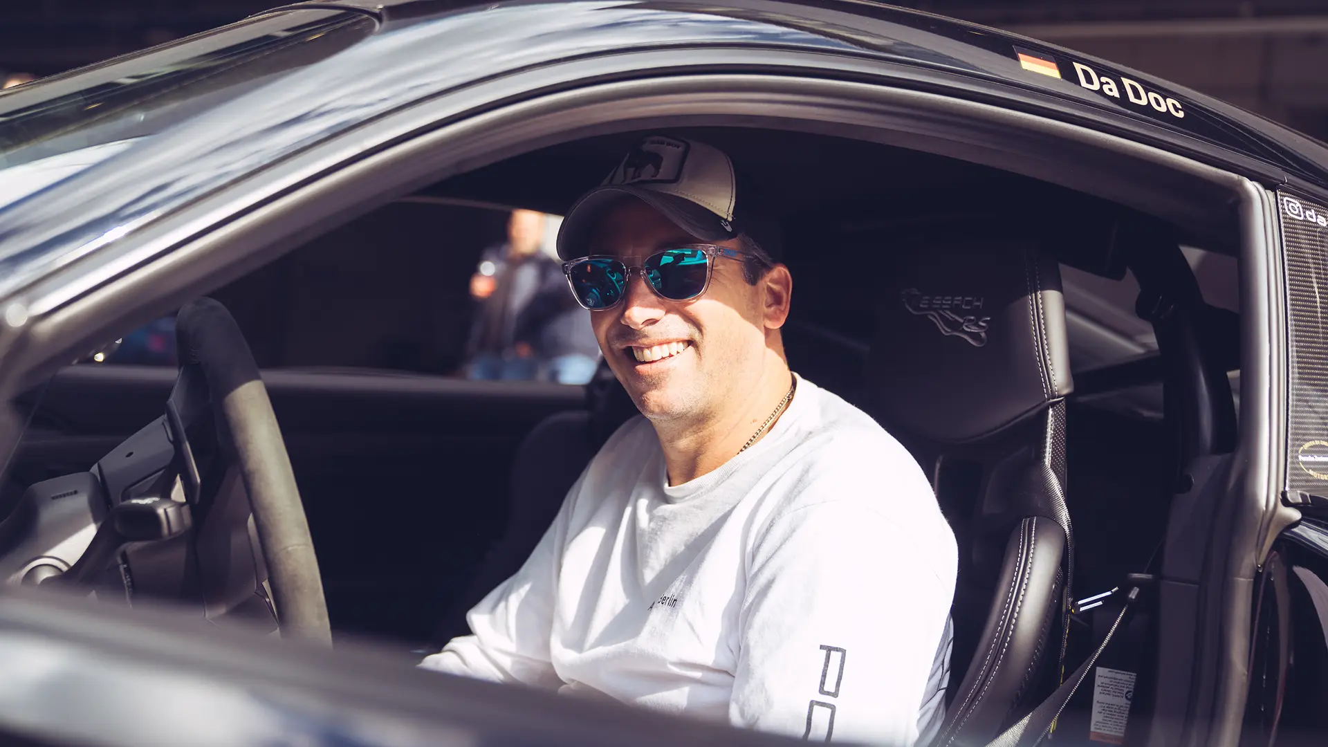 Trackday-Teilnehmer sitzt lächelnd im Porsche-Cockpit mit Rennschalen-Sitzen auf der Rennstrecke