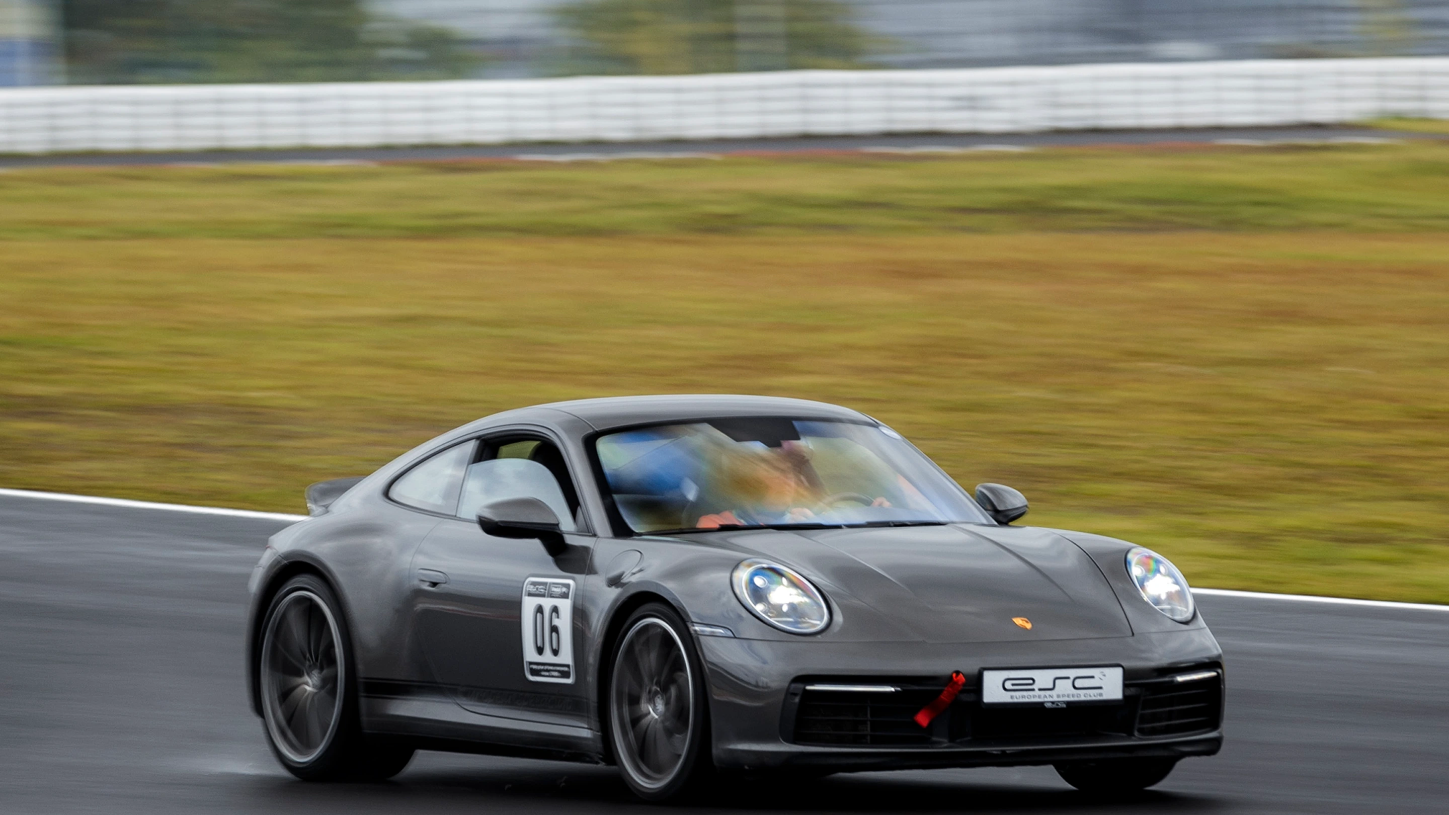 Grauer Porsche 992 mit ESC-Branding und Startnummer fährt mit hoher Geschwindigkeit auf der Rennstrecke beim Trackday