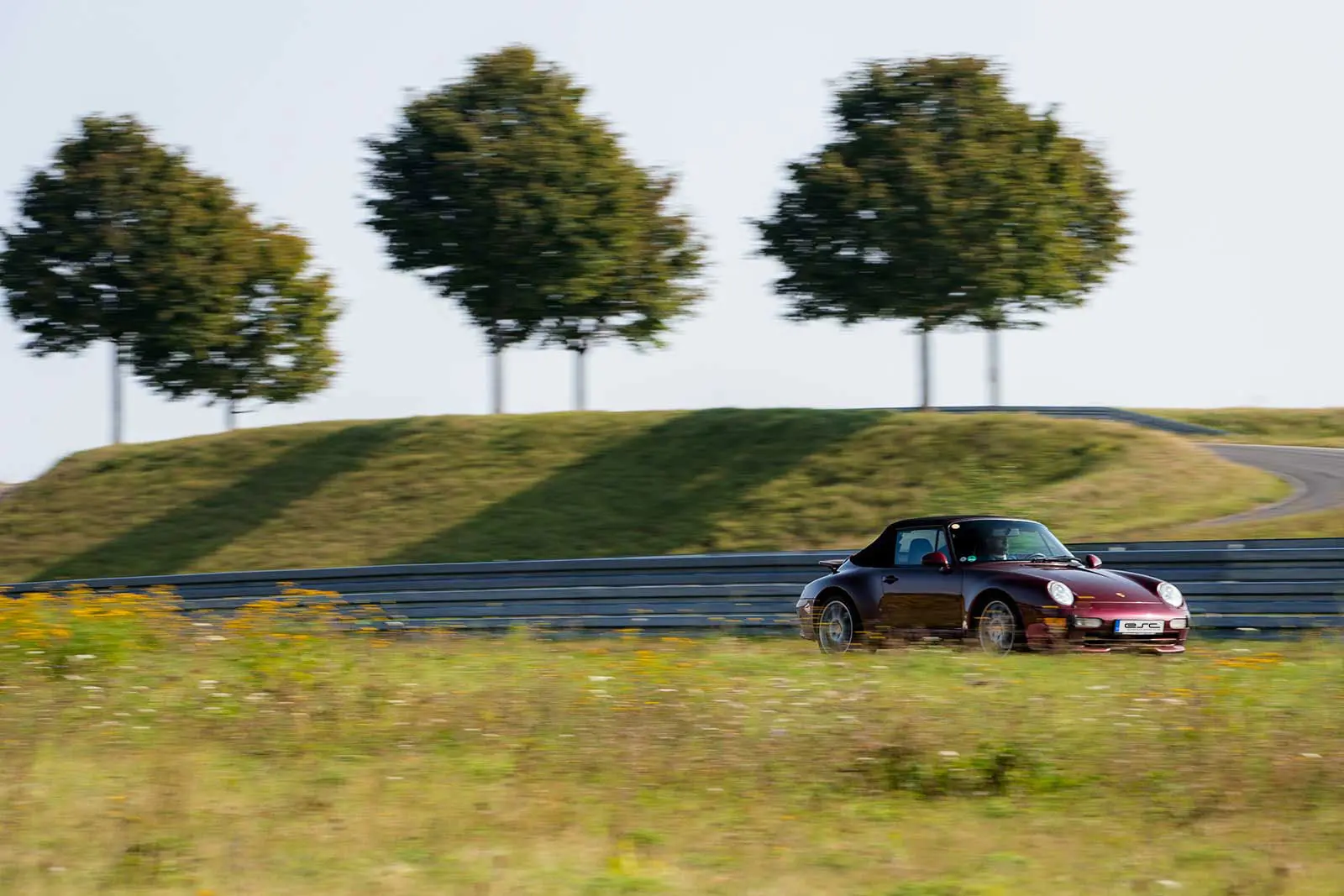 Klassischer Porsche 993 Cabriolet in Bordeauxrot auf dem idyllischen Handling-Kurs der Boxberg Rennstrecke