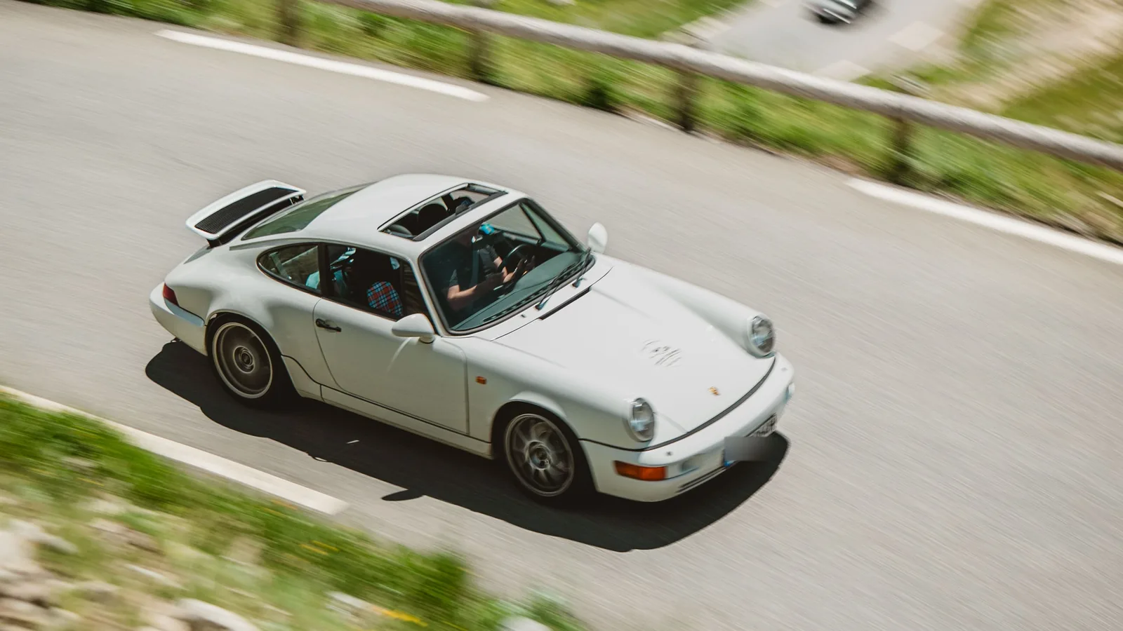 Klassischer weißer Porsche 964 in Bewegung auf einer alpinen Serpentinenstraße bei der Grand-Touring-Reise Grand Le Mans