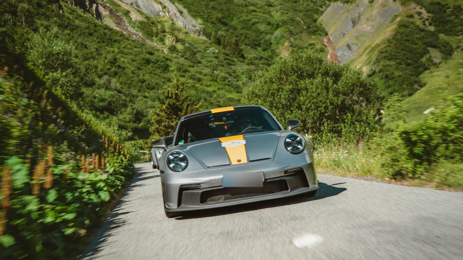 Grauer Porsche 911 GT3 auf einer französischen Alpenstraße mit grünen Bergen bei Grand Le Mans