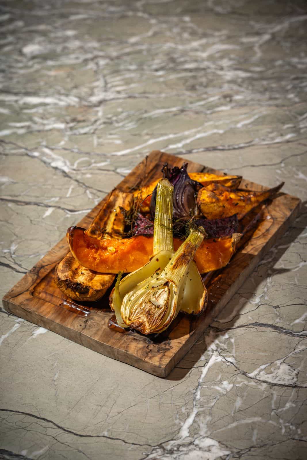 Close-up of a person cutting into a breaded meat dish served on a small wooden table, accompanied by thin fries and garnished with herbs