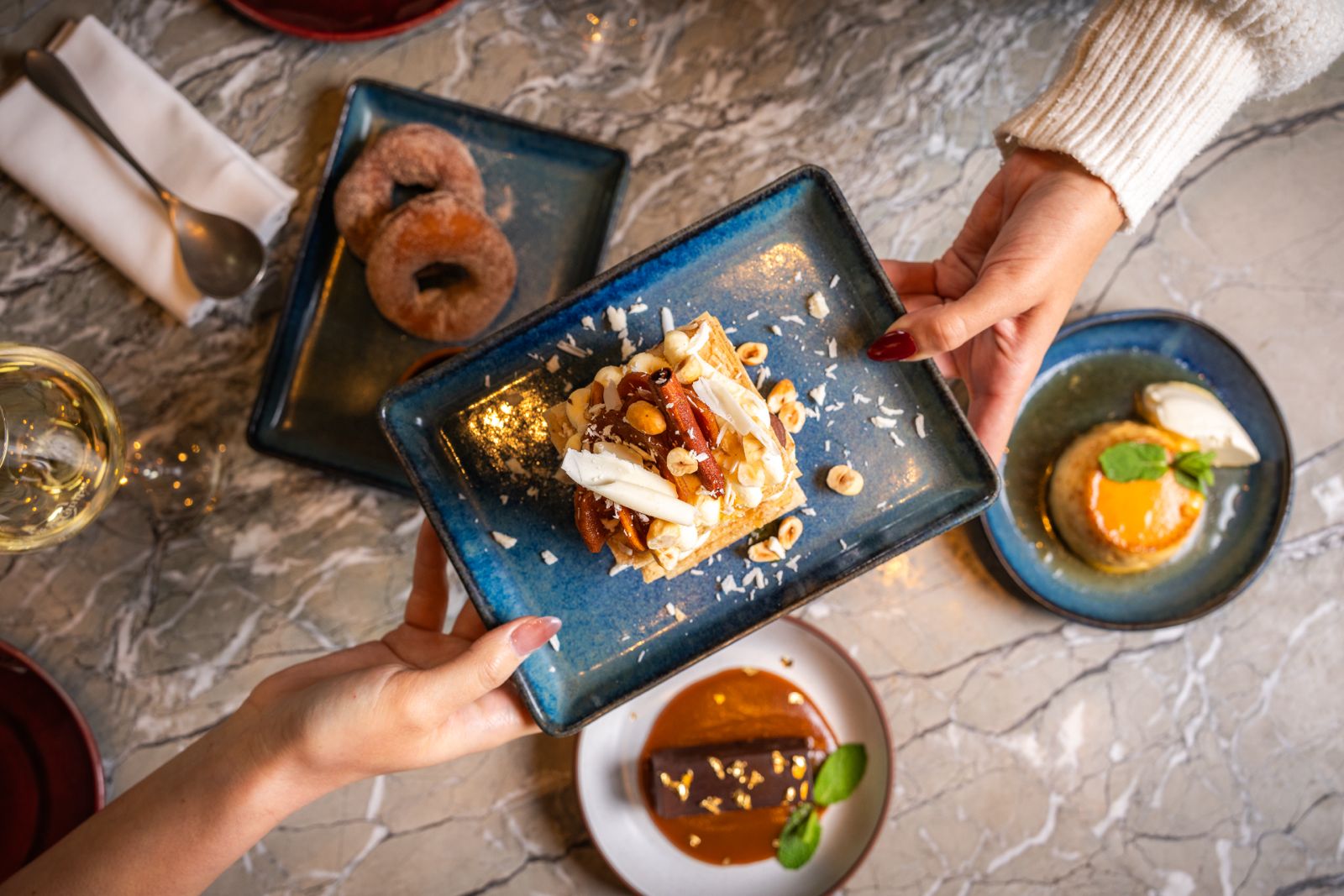 Glass and pitcher of red sangria with citrus slices and ice, next to a small vase with fresh flowers