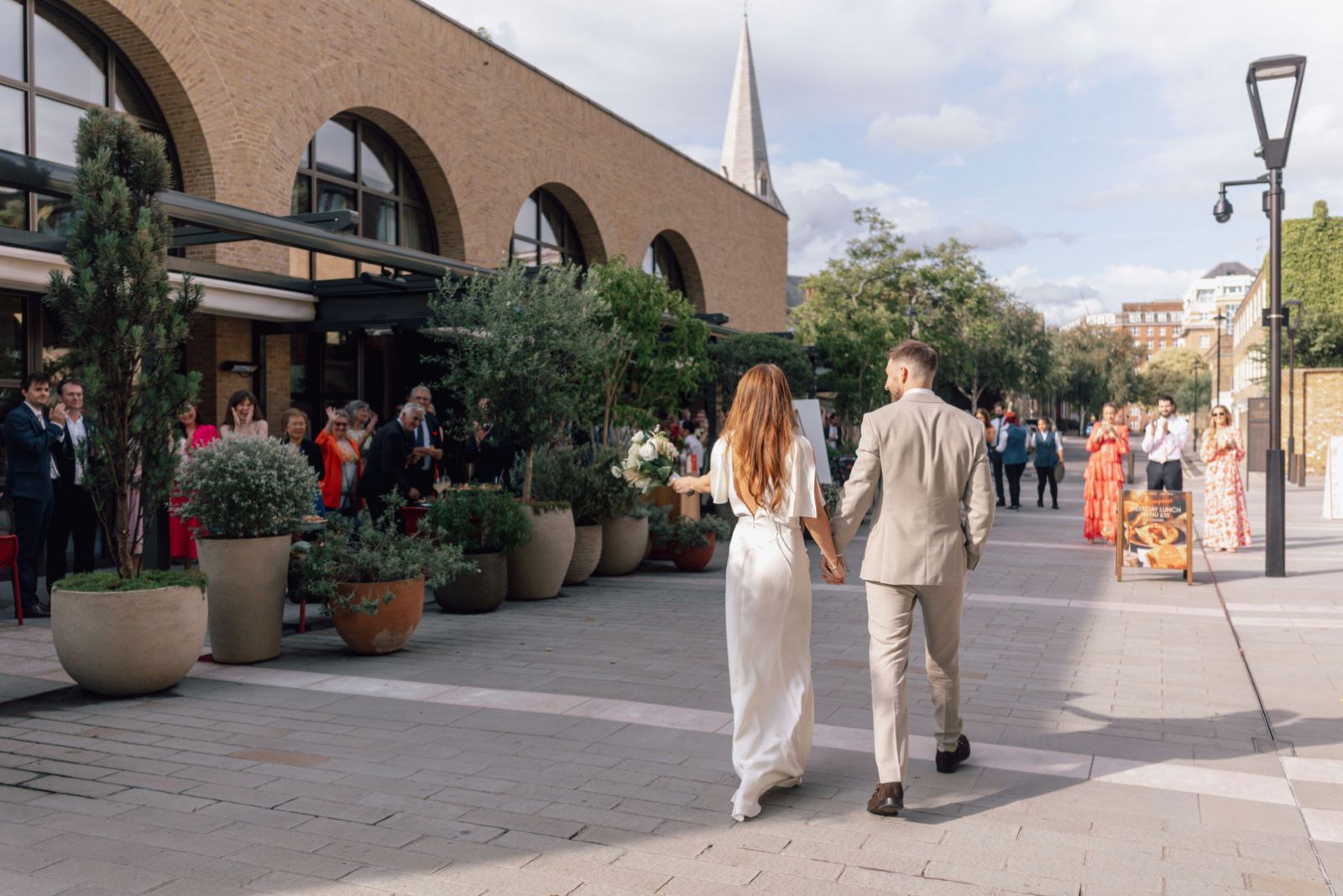 Sunlit indoor dining space with patterned benches, wooden tables, and an olive tree surrounded by lush greenery